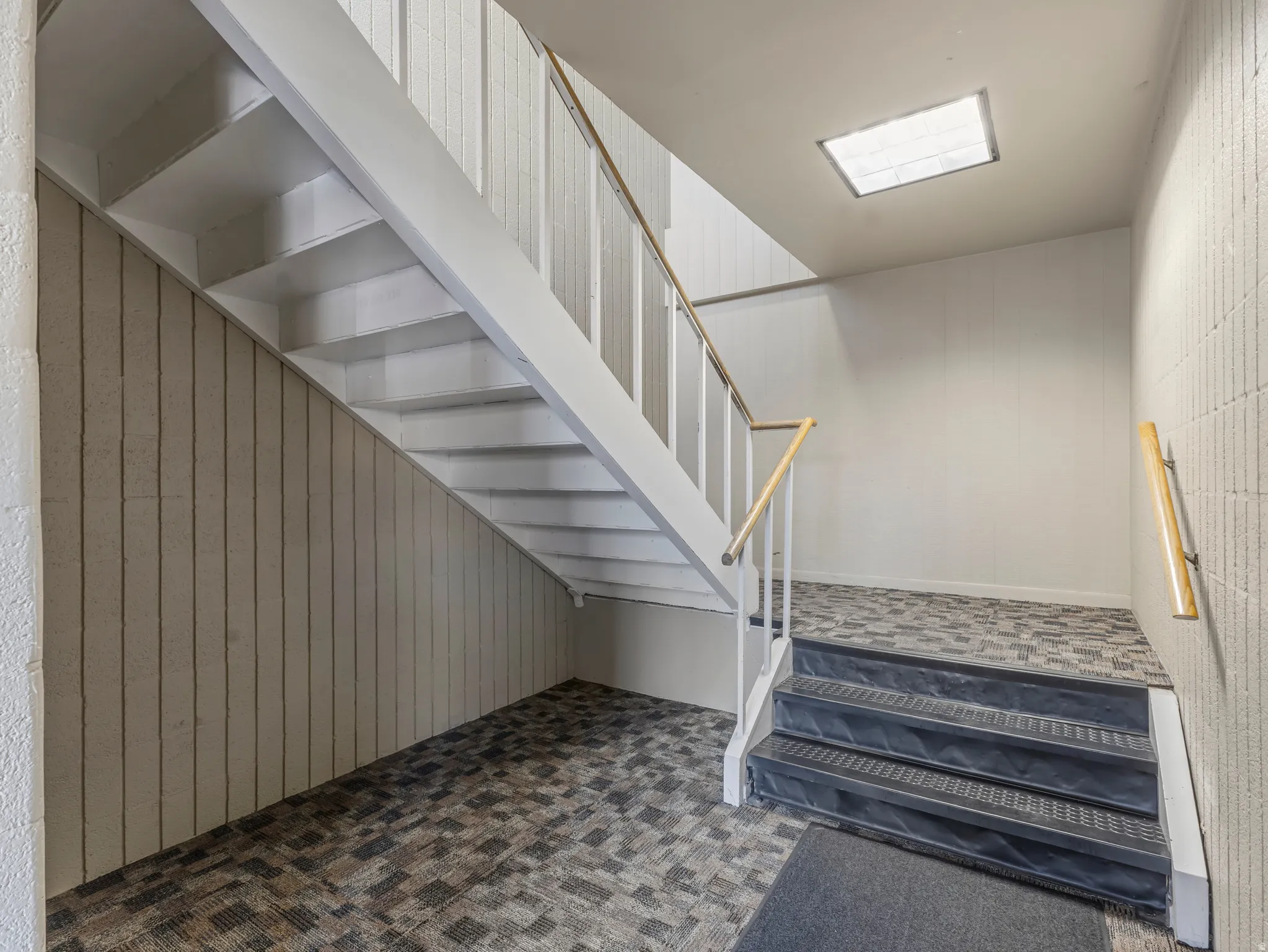 Stairwell featuring multi-toned carpet flooring, white painted stairs, and a white balustrade with wood railing