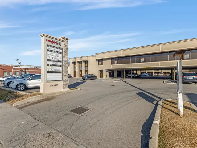 Commercial building featuring a stone and stucco monument sign, a paved parking area, and an integrated covered parking structure