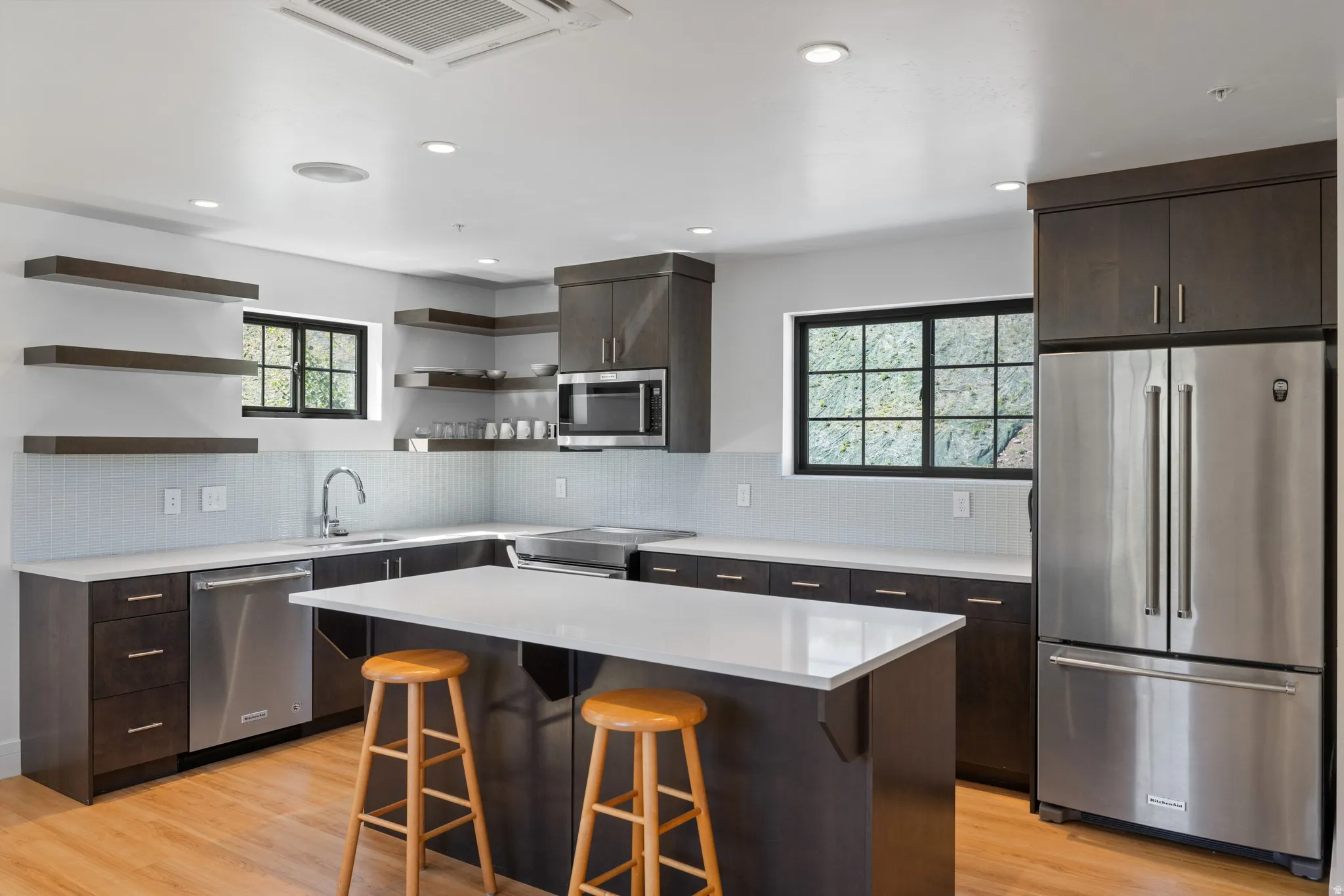 Modern kitchen featuring dark wood-finish cabinetry, stainless steel appliances, a center island with a light-toned countertop, wood-finish flooring, and recessed lighting