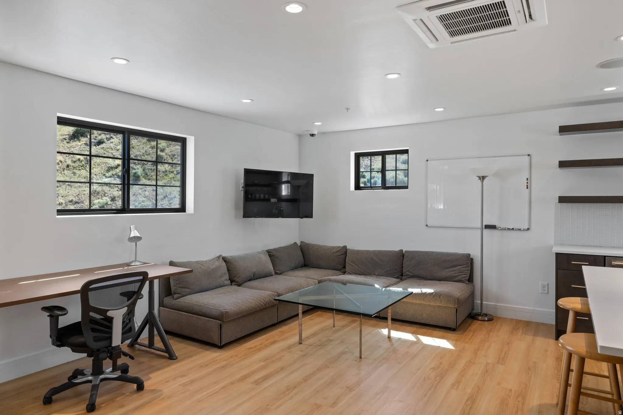 Open-concept living space with light wood-finish flooring, recessed lighting, white walls, and black-framed windows