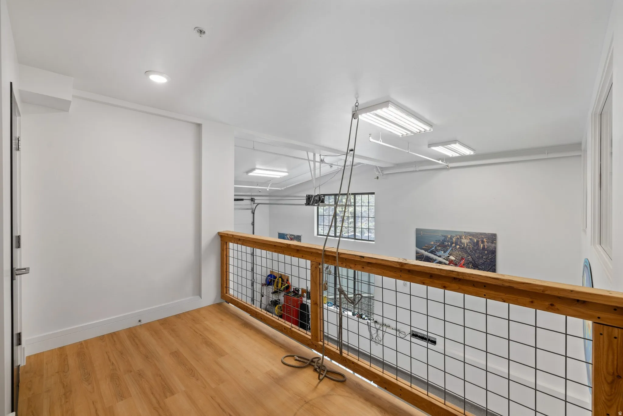 Mezzanine with wood-finish flooring, metal grid railing with wood top rail, recessed ceiling lighting, and a white interior door