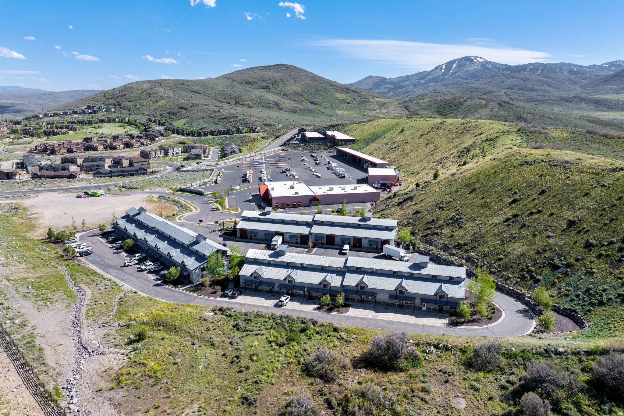 Multi-building complex featuring varied architectural styles with pitched and flat roofs, surrounded by undulating green hills