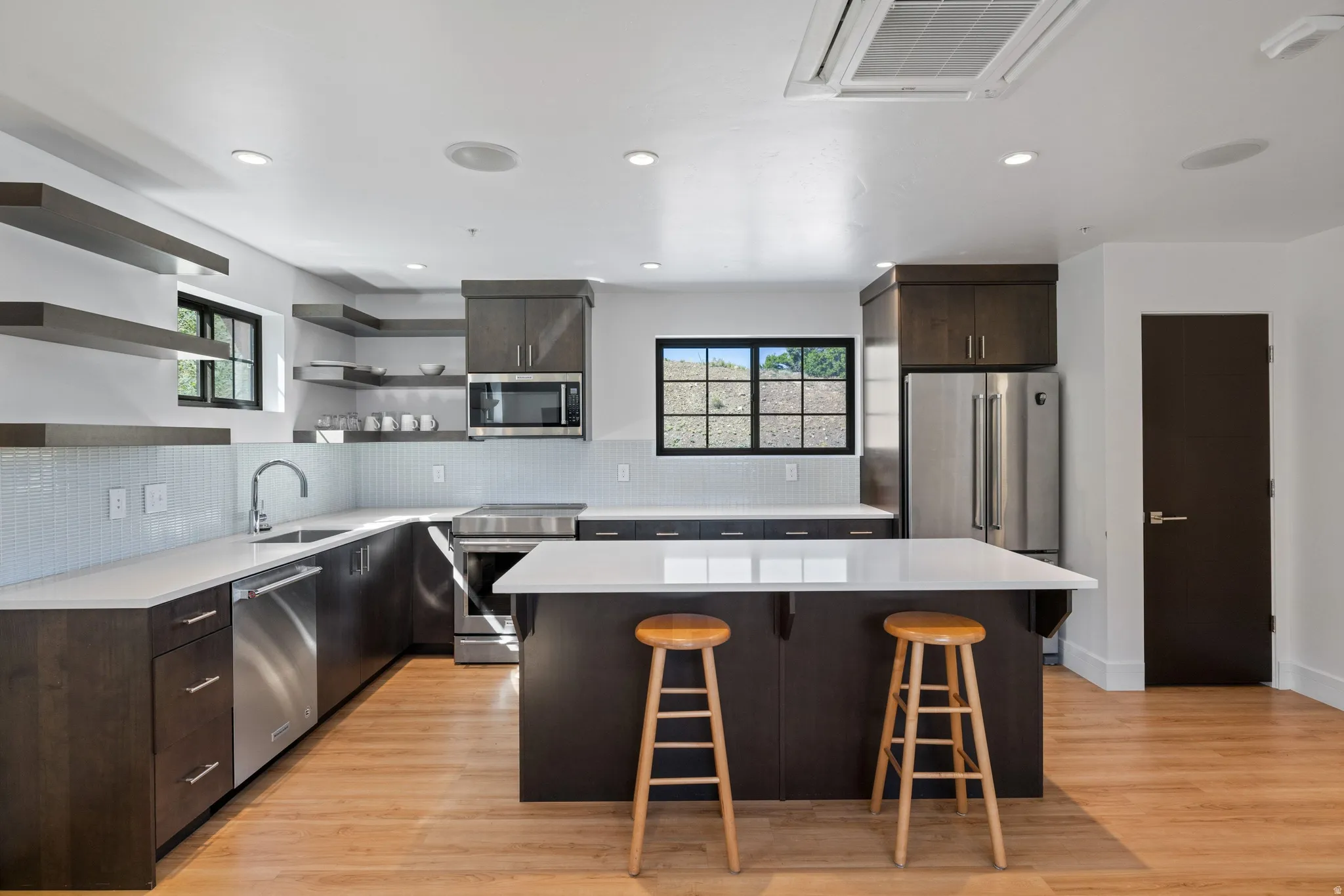 Modern kitchen featuring light wood-finish flooring, dark wood cabinetry, white countertops, and a white subway tile backsplash