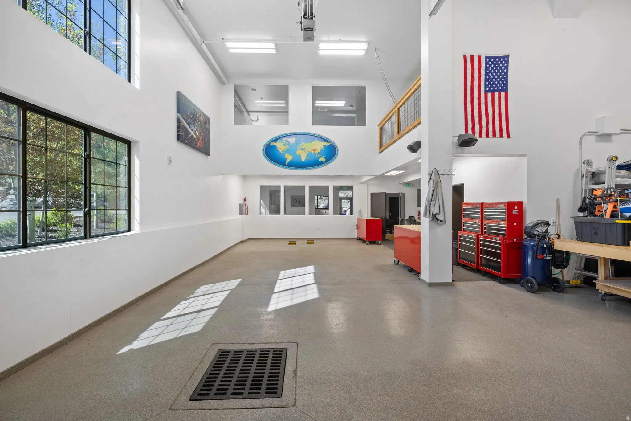 Spacious multi-purpose room featuring high ceilings with upper windows, large gridded windows, light-colored flooring, and a mezzanine balcony