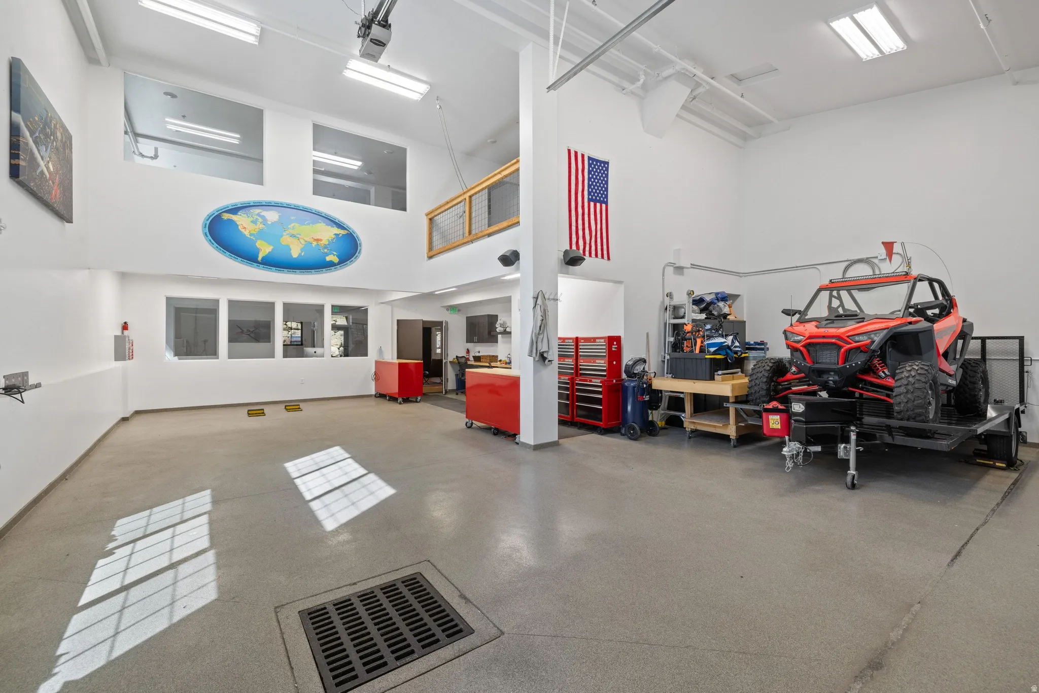 Spacious garage with high ceilings, polished concrete flooring, extensive built-in lighting, an integrated floor drain, and multiple wall-mounted windows providing natural illumination