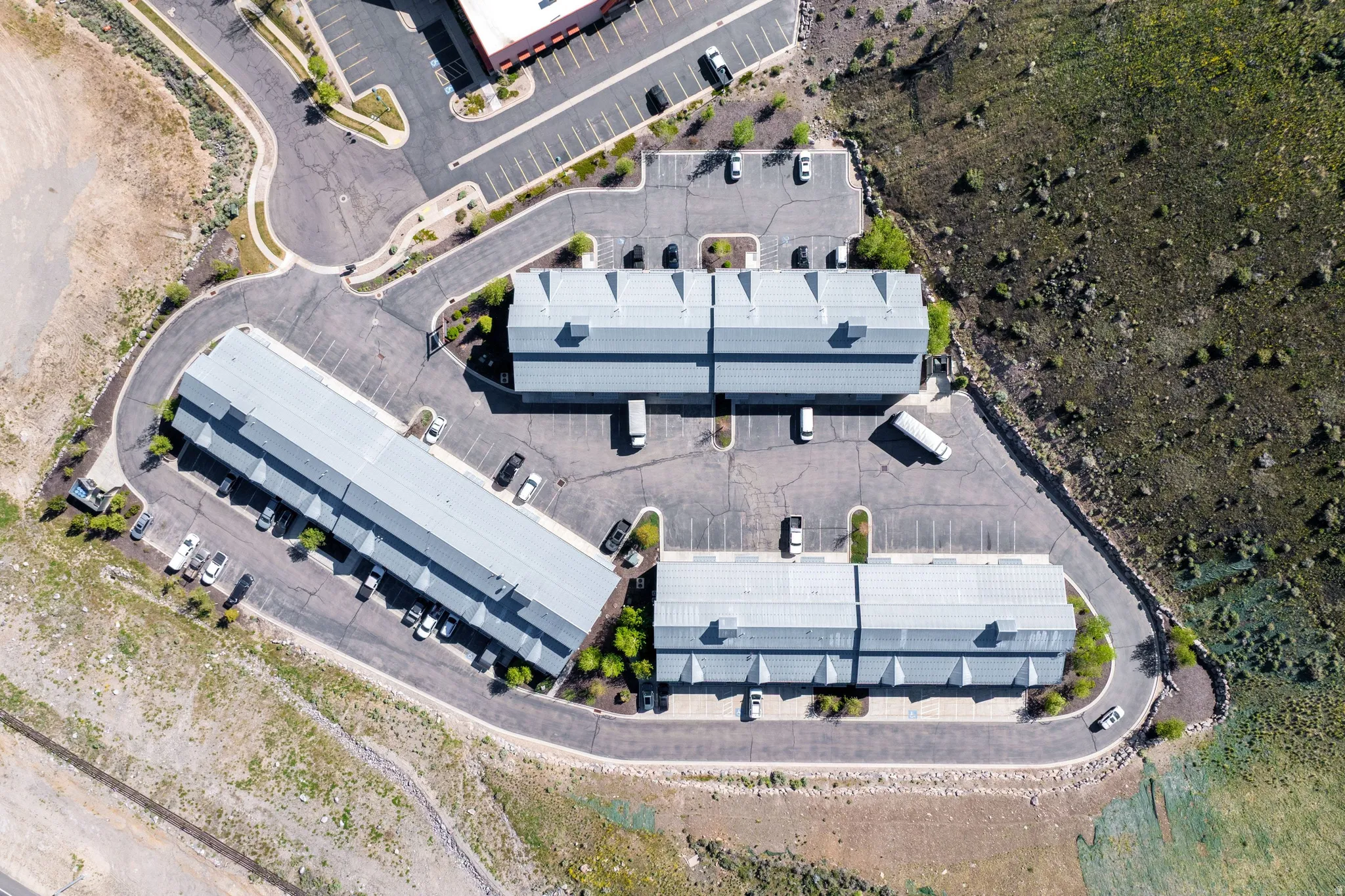 Aerial perspective showcasing multiple buildings with light-colored roofs, surrounded by extensive paved parking areas