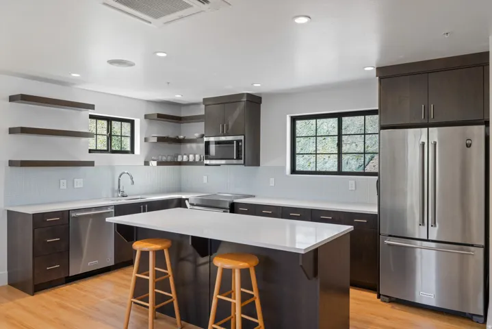 Modern kitchen featuring dark wood-finish cabinetry, stainless steel appliances, a center island with a light-toned countertop, wood-finish flooring, and recessed lighting