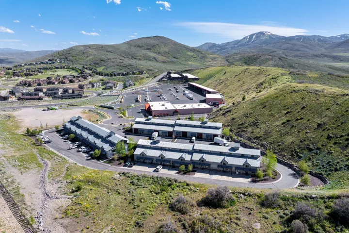 Multi-building complex featuring varied architectural styles with pitched and flat roofs, surrounded by undulating green hills