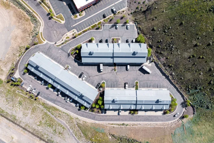 Aerial perspective showcasing multiple buildings with light-colored roofs, surrounded by extensive paved parking areas