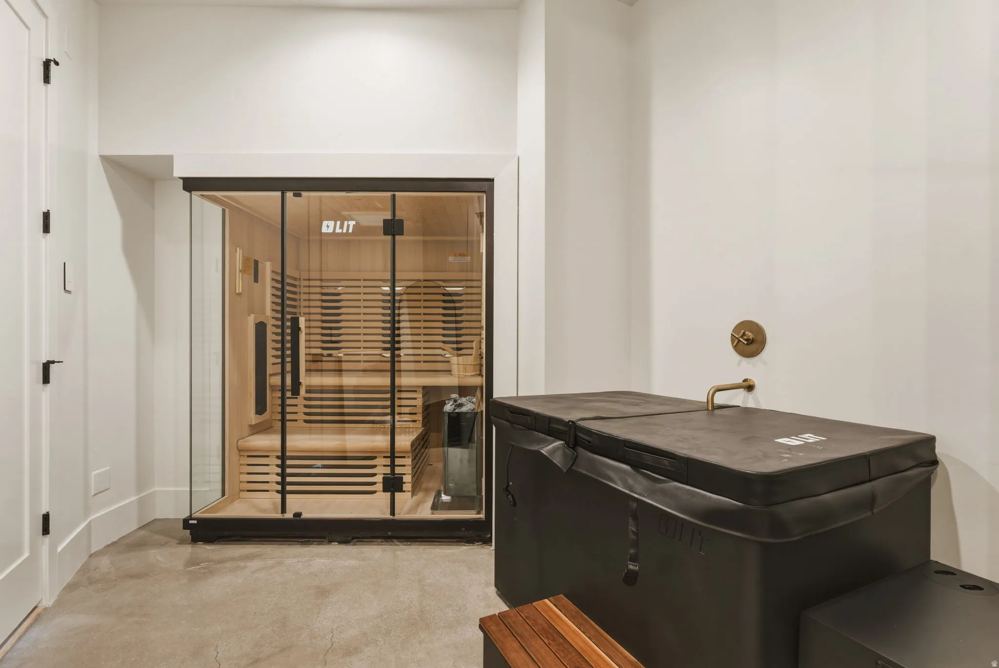 Glass-enclosed sauna featuring light wood paneling and bench seating along side of the cold plunge and full shower.