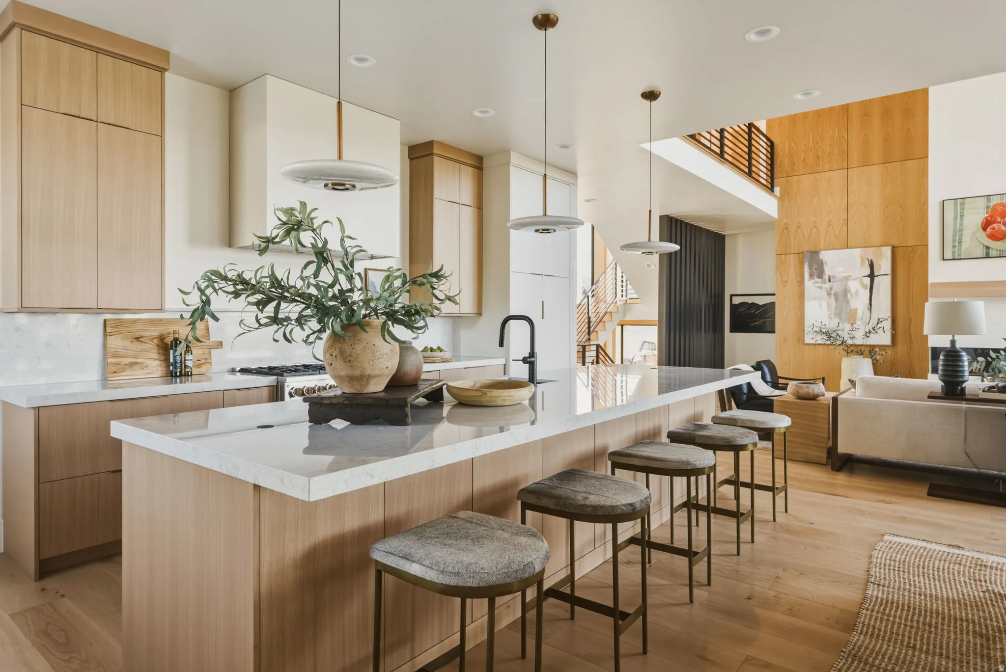 Open-concept kitchen featuring an oversized island with seating, integrated sink, and contemporary pendant lighting