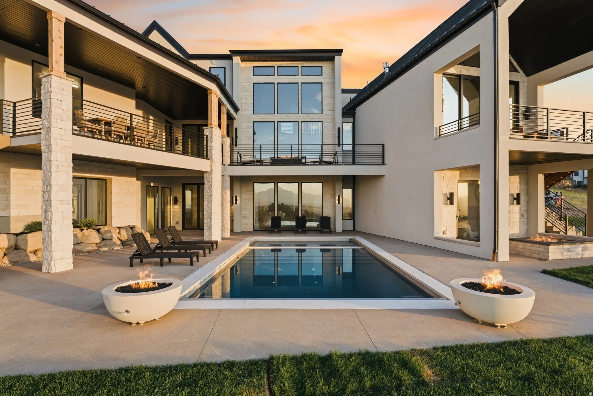 Expansive backyard oasis featuring an in-ground swimming pool, two contemporary fire pits, and a built-in stone fire pit