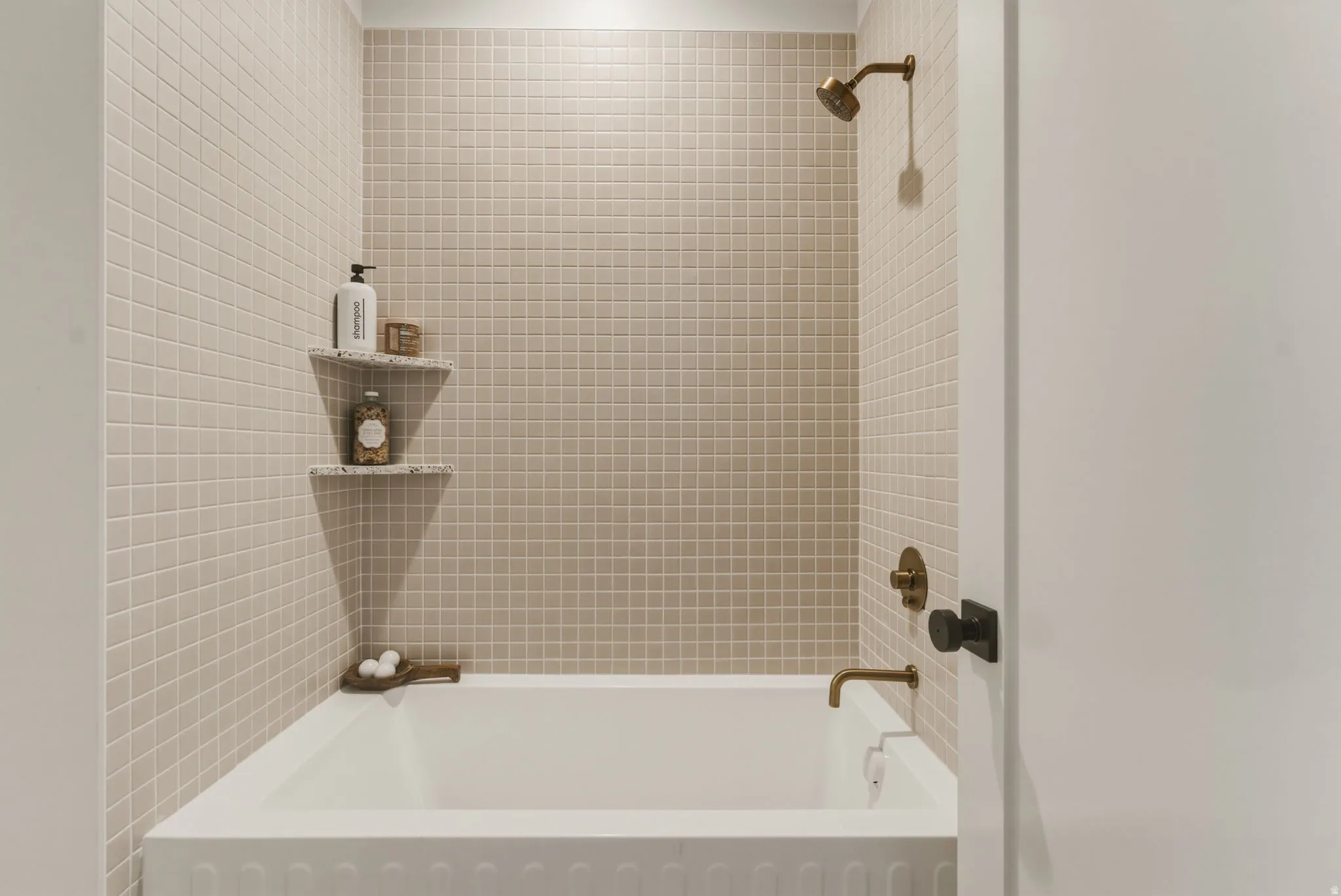 Tub and shower combination featuring floor-to-ceiling square tile, bronze-finish fixtures, and built-in corner shelving
