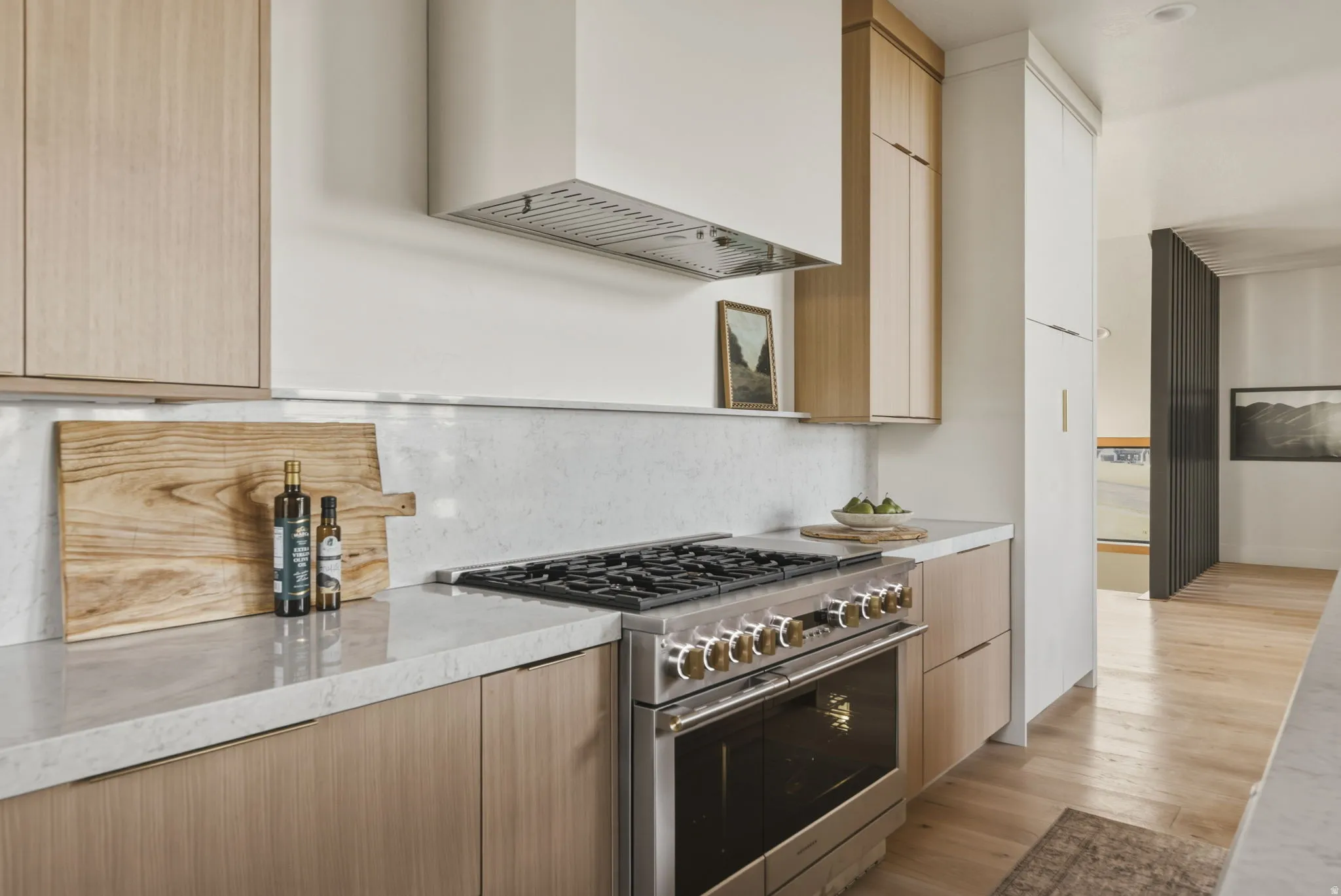Stainless steel range with gold-toned hardware under a contemporary range hood