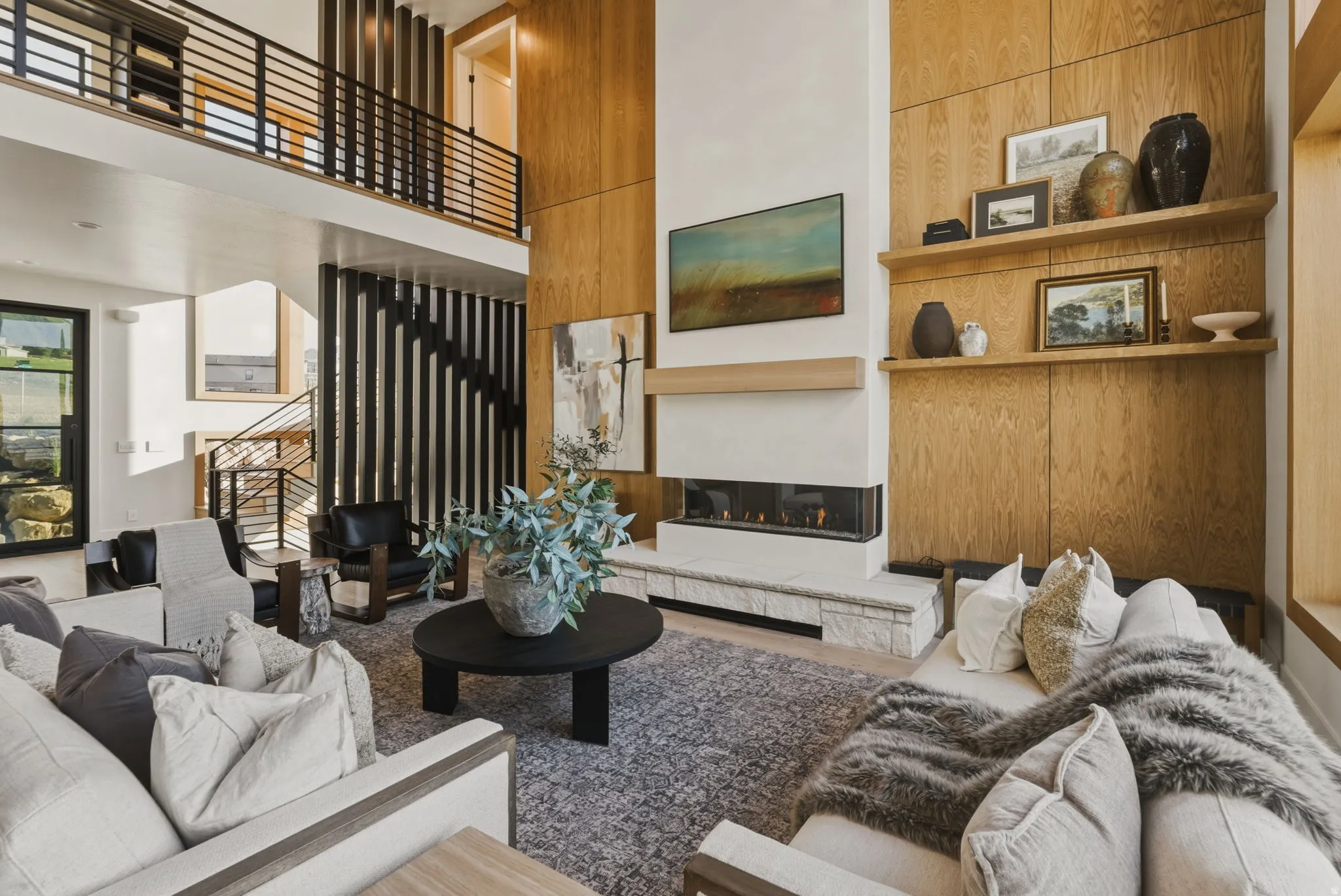 Two-story living area featuring a linear fireplace with a stone hearth, wood-paneled accent walls, and a multi-level open-tread staircase with metal railings