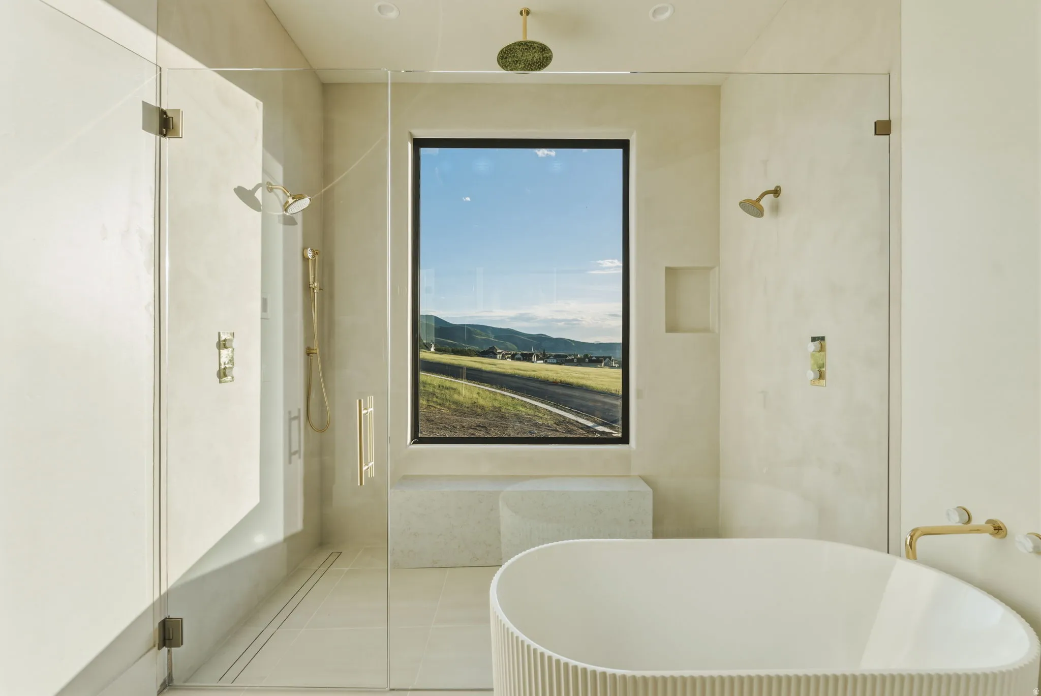 Freestanding soaking tub with fluted exterior, walk-in shower with dual shower heads, and large window showcasing mountain scenery
