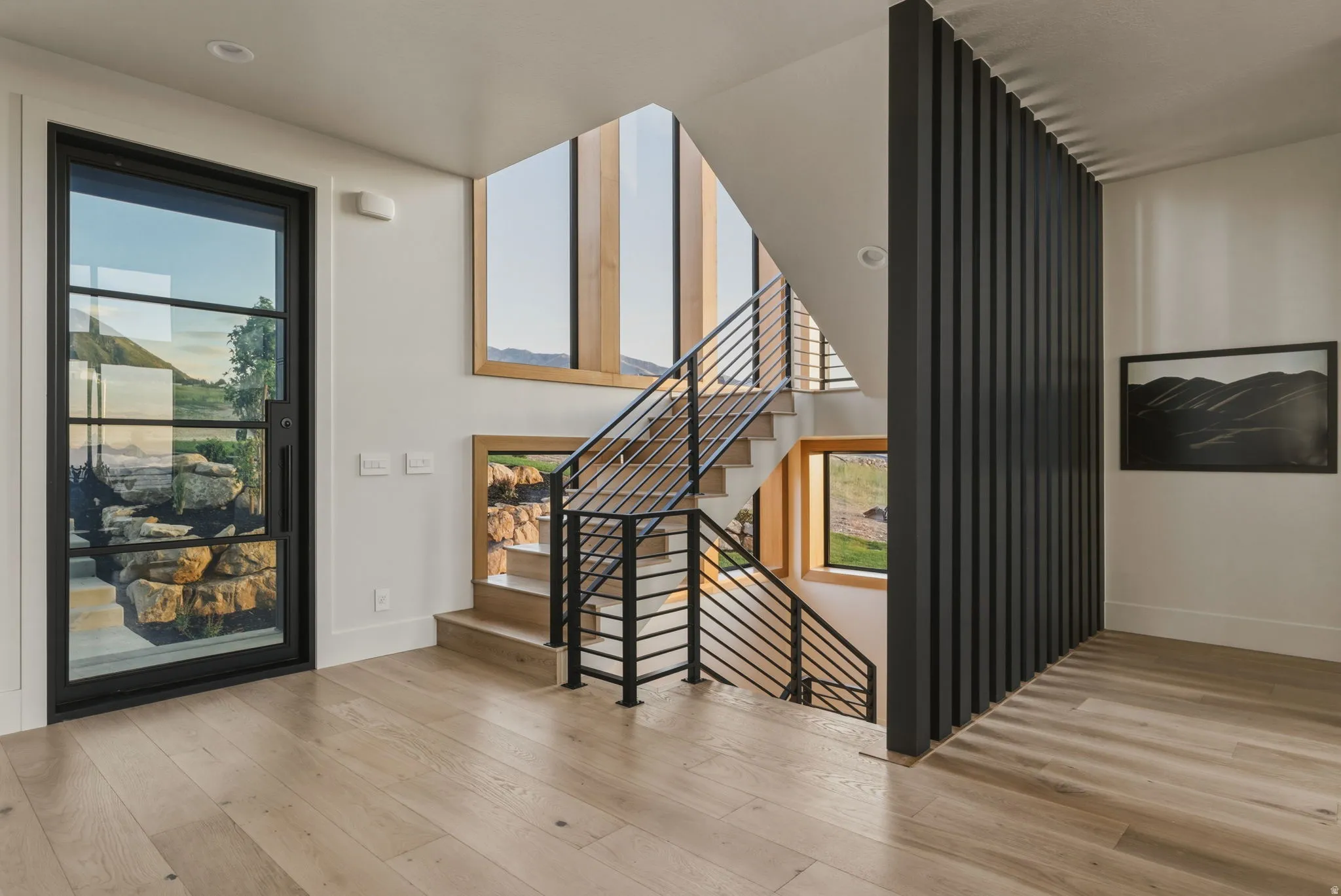 Contemporary entryway featuring a black-framed glass entry door, light wood-finish flooring, and a multi-level staircase with metal railings