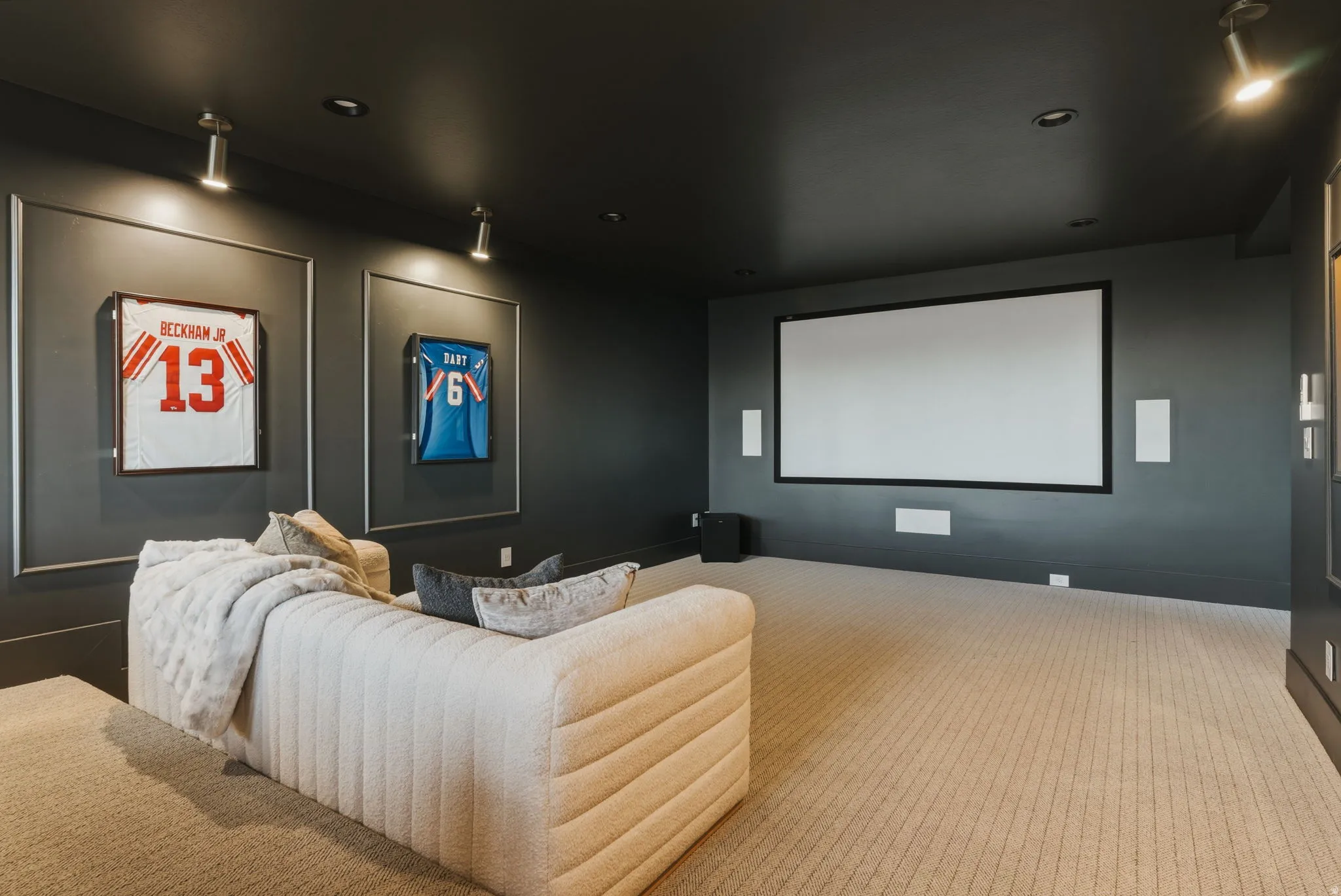 Dedicated media room featuring a large projector screen, built-in wall speakers, and recessed ceiling lighting