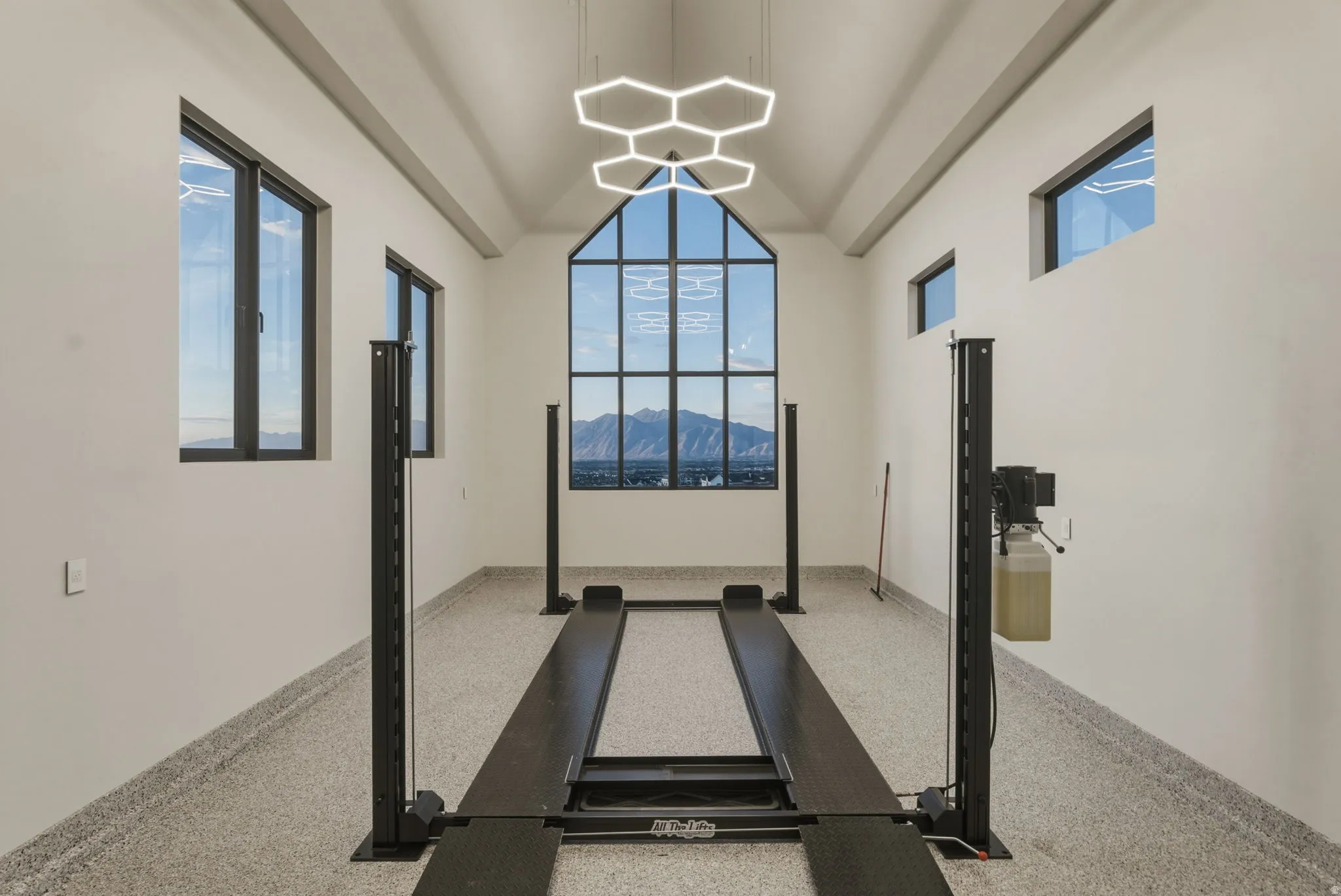 Automotive lift system within a spacious garage featuring a vaulted ceiling and an expansive multi-pane window framing a mountain backdrop