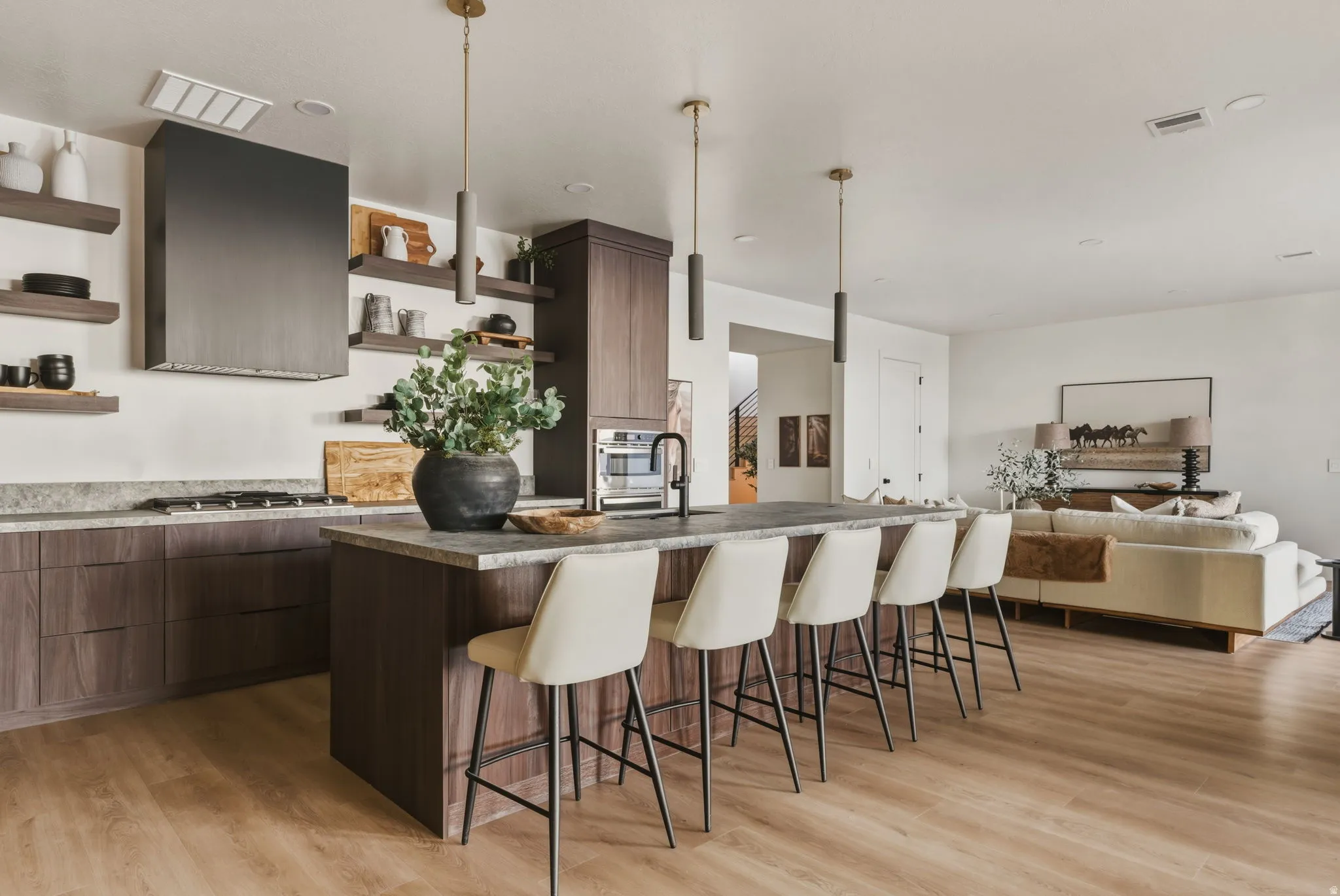 Open-concept kitchen featuring dark wood-finish cabinetry, stone countertops, a large center island with pendant lighting, and light wood-finish flooring