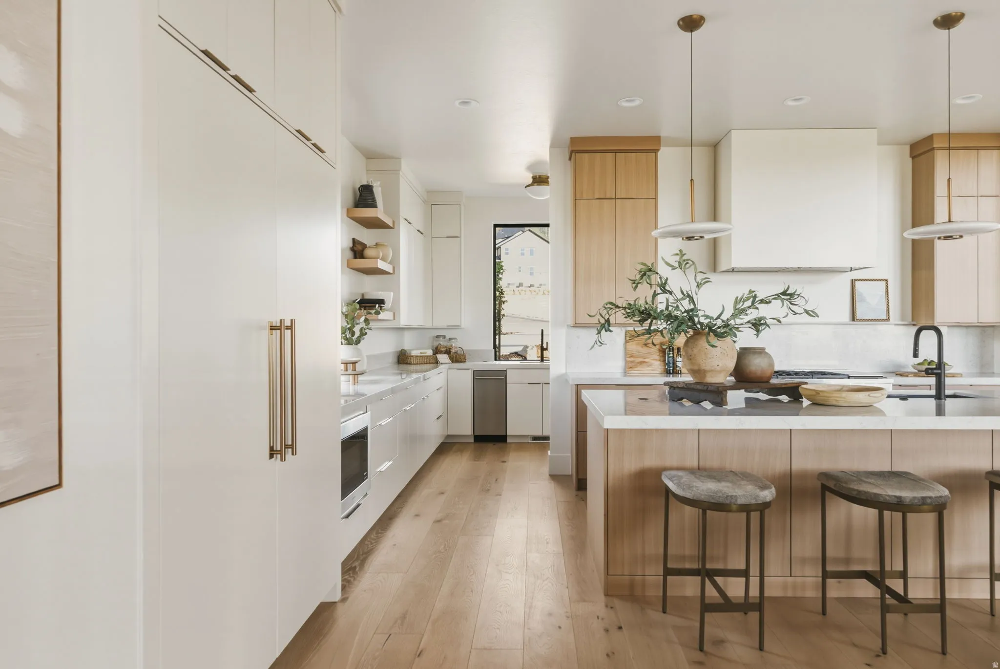 Open-concept kitchen featuring light wood-finish flooring, a central island with countertop seating, white and light wood-finish cabinetry, integrated appliances, and a range hood