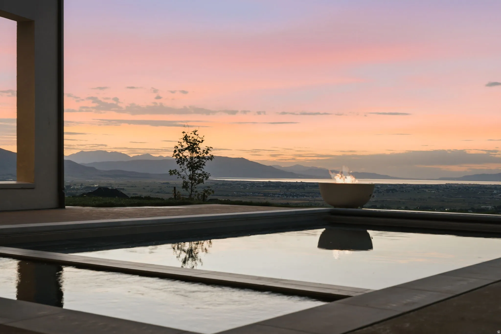 Outdoor water feature with stone coping, a built-in fire bowl, and a distant mountain and water backdrop