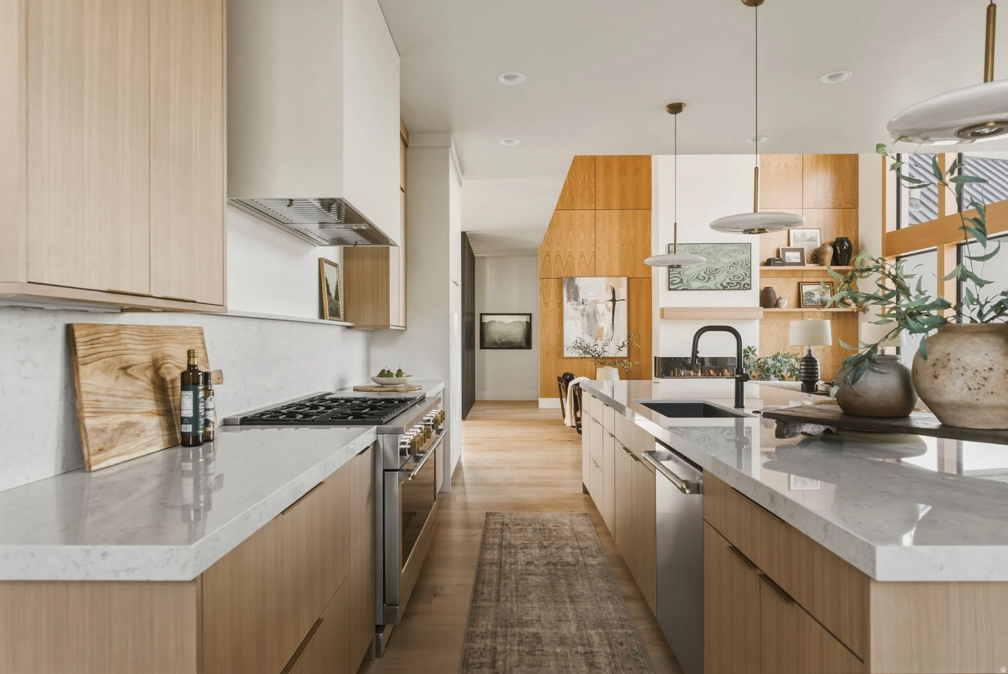 Open-concept kitchen featuring light wood-finish cabinetry, stone countertops, and a stainless steel gas range with a matching range hood