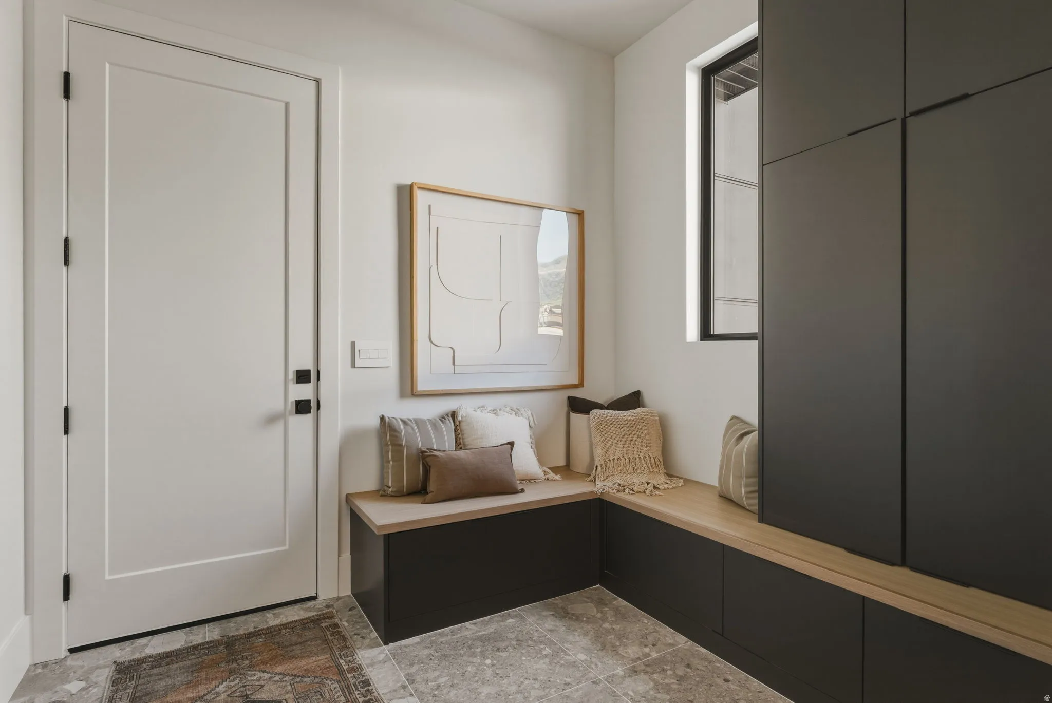 Integrated mudroom storage featuring dark cabinetry, natural wood-finish bench seating, and a large window