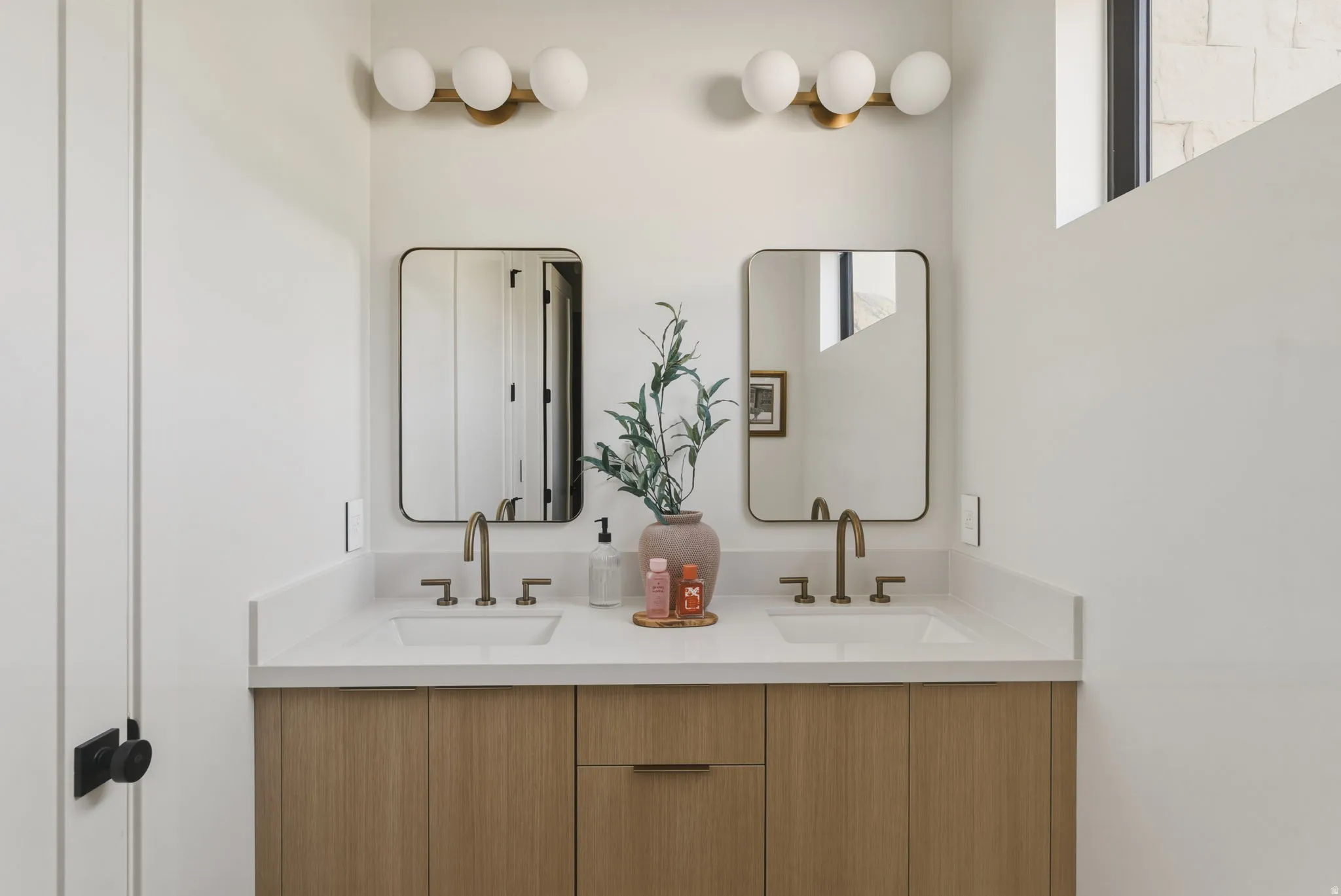 Dual vanity with wood-finish cabinetry, white countertops, and matte gold-tone fixtures
