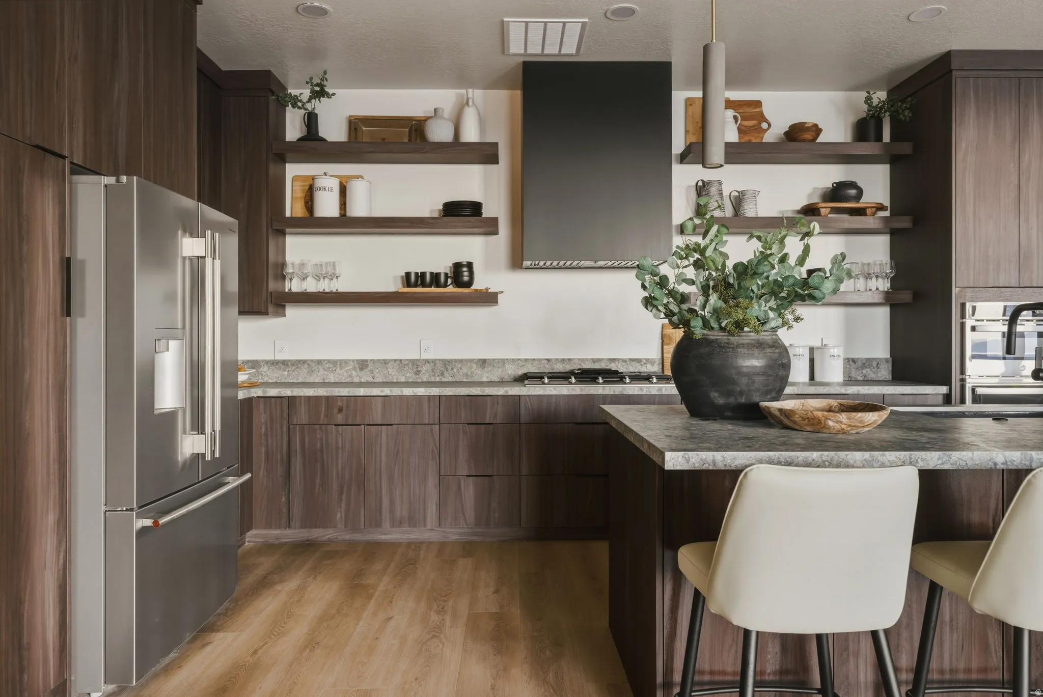 Contemporary kitchen featuring wood-finish cabinetry, stainless steel refrigerator, dark range hood, and open shelving