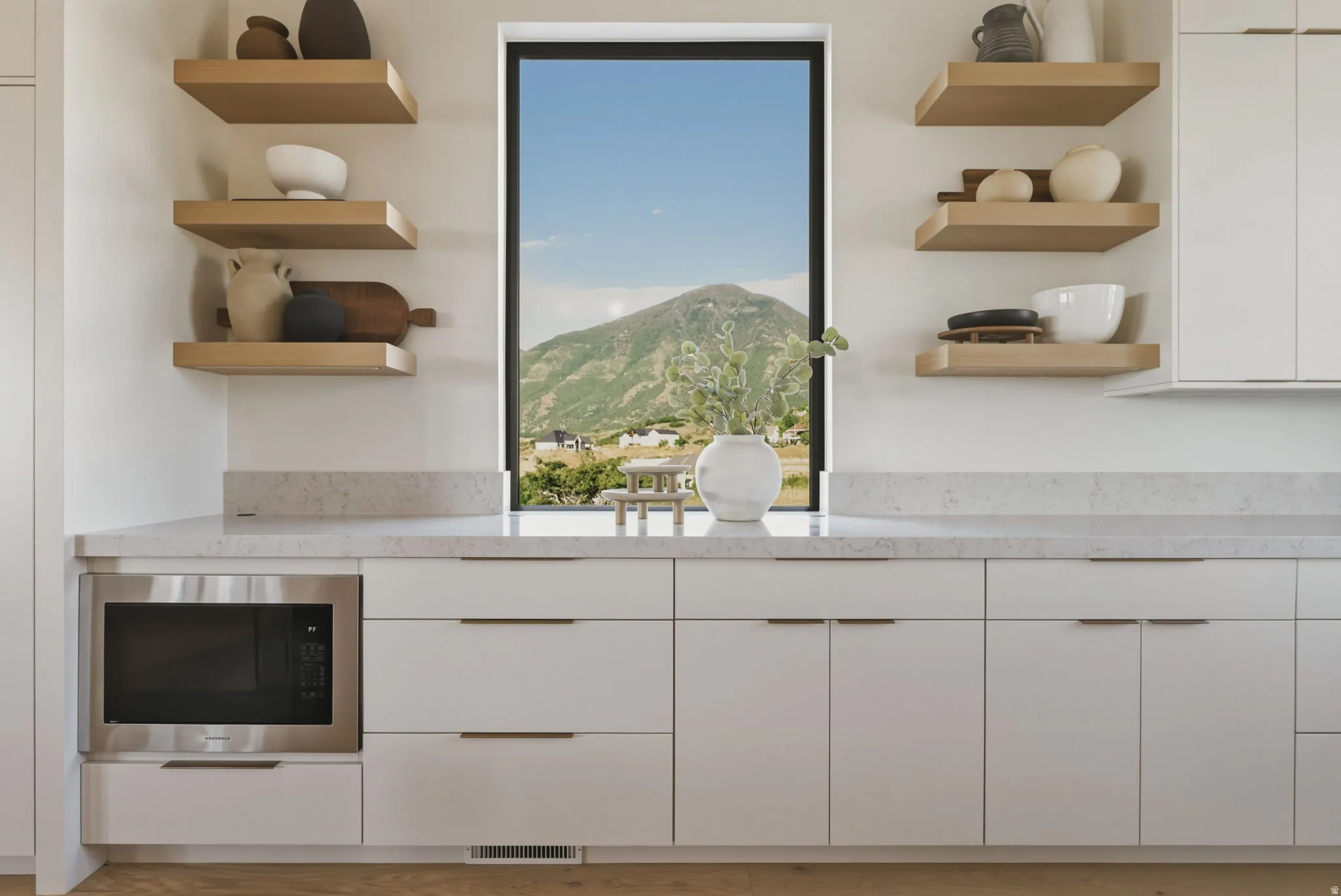 Modern kitchen cabinetry featuring a built-in microwave, light-toned countertops, and floating wood shelves