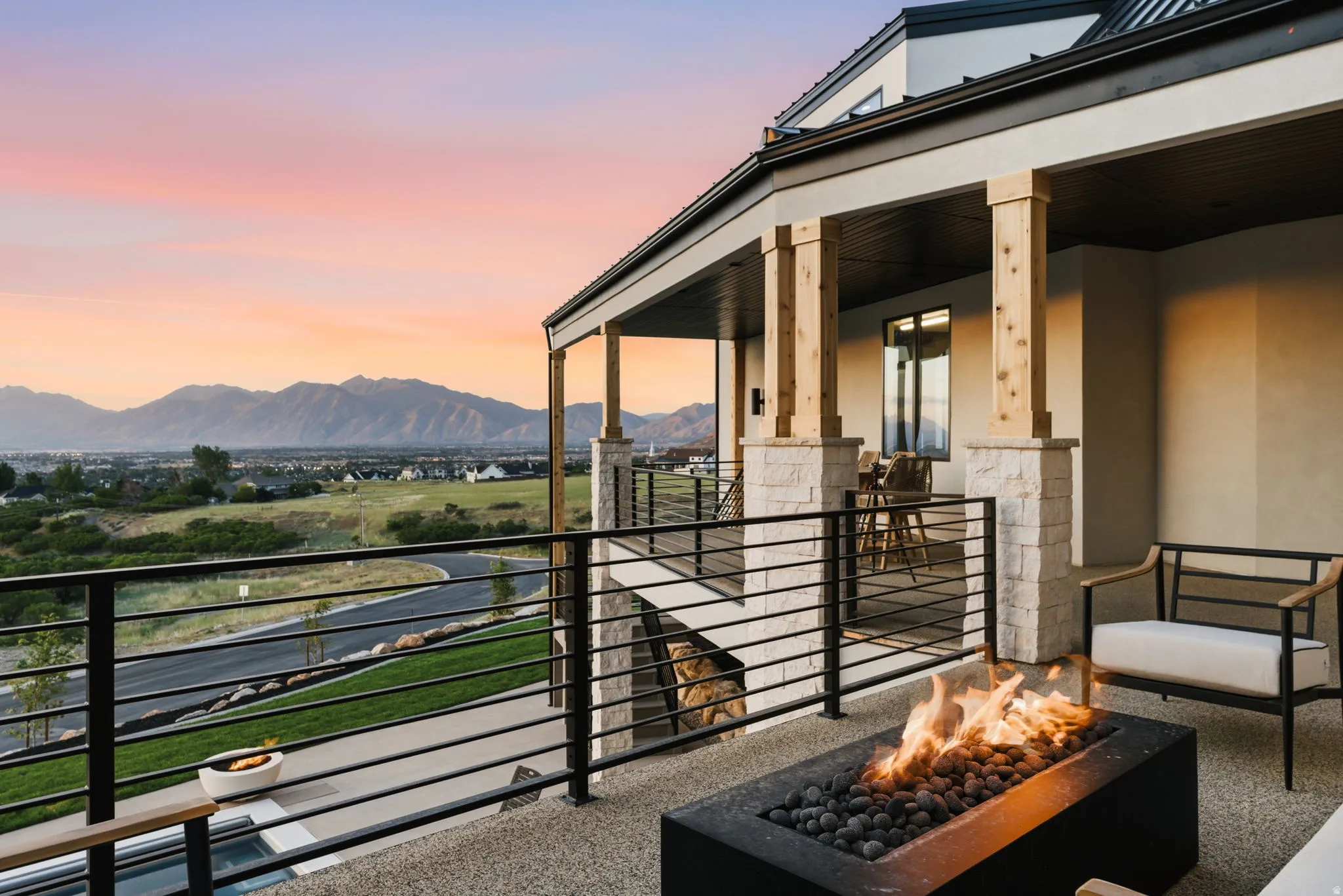 Expansive outdoor patio featuring a built-in fire pit with lava rocks, durable stone tile flooring, and a contemporary black metal railing