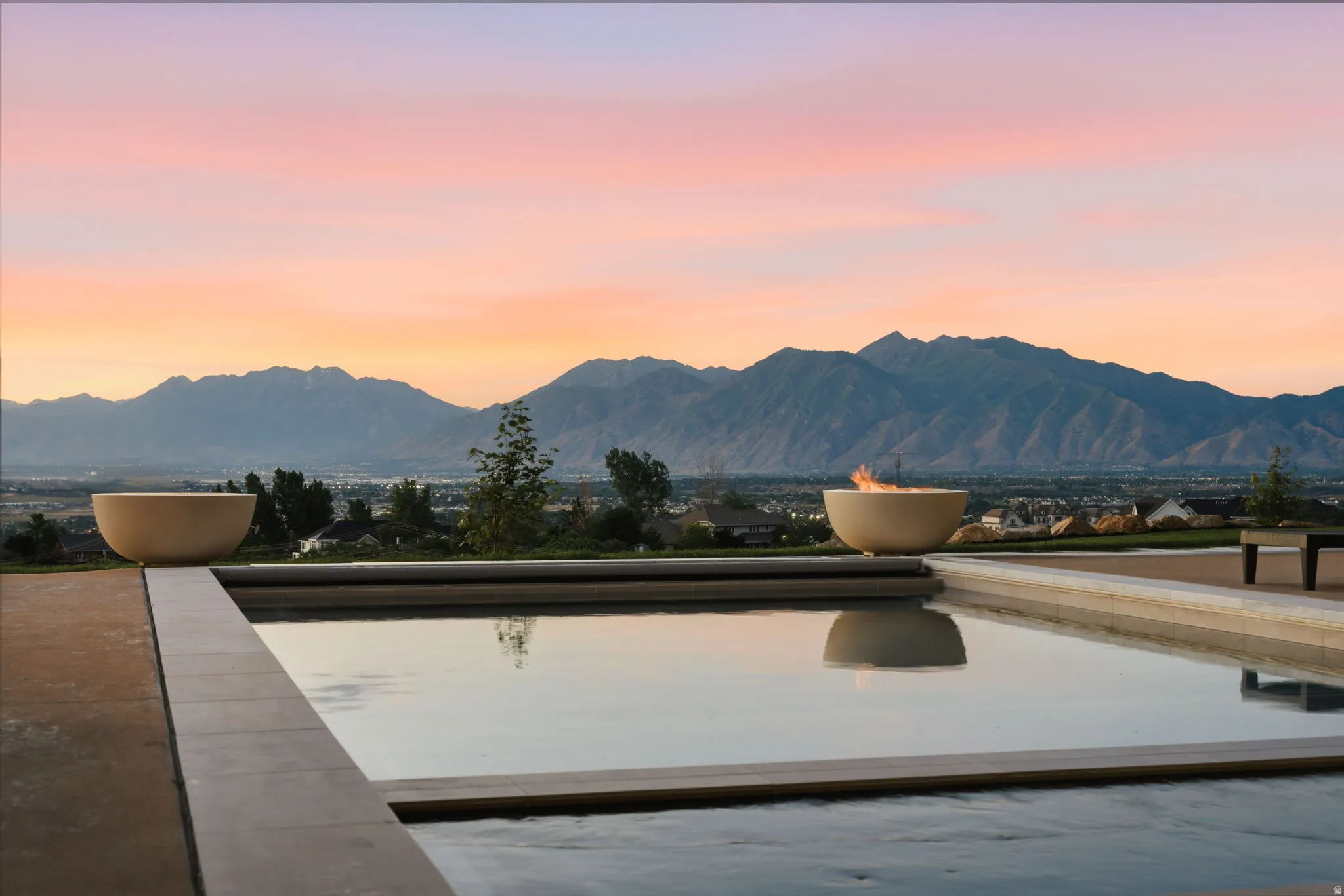 Outdoor pool with surrounding hardscape, two decorative fire bowls, and a mountain backdrop