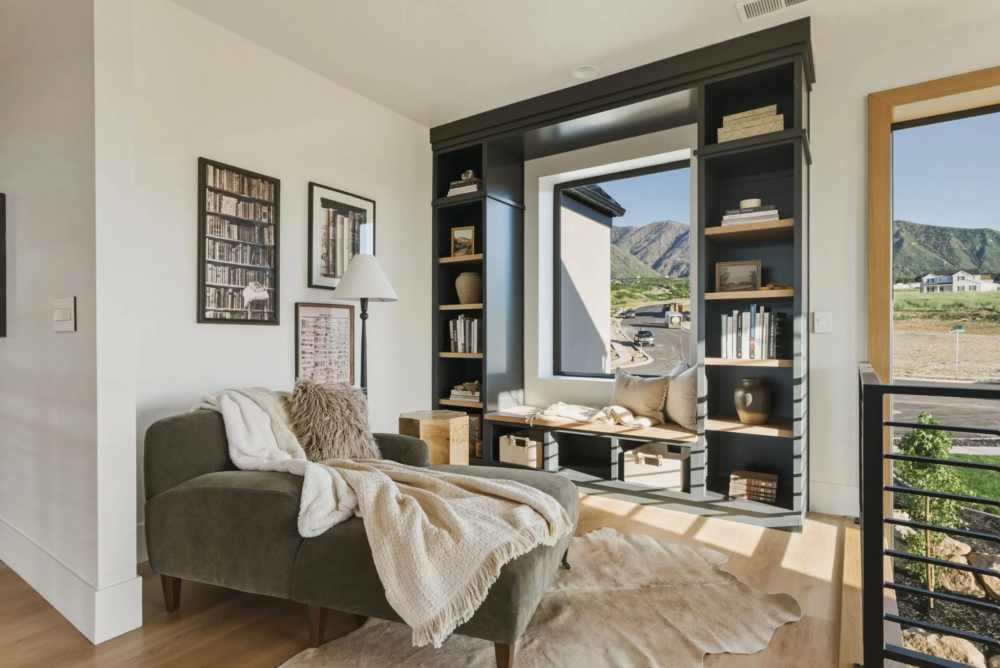 Built-in shelving unit with a window bench, light wood-finish flooring, white walls, and a black metal railing