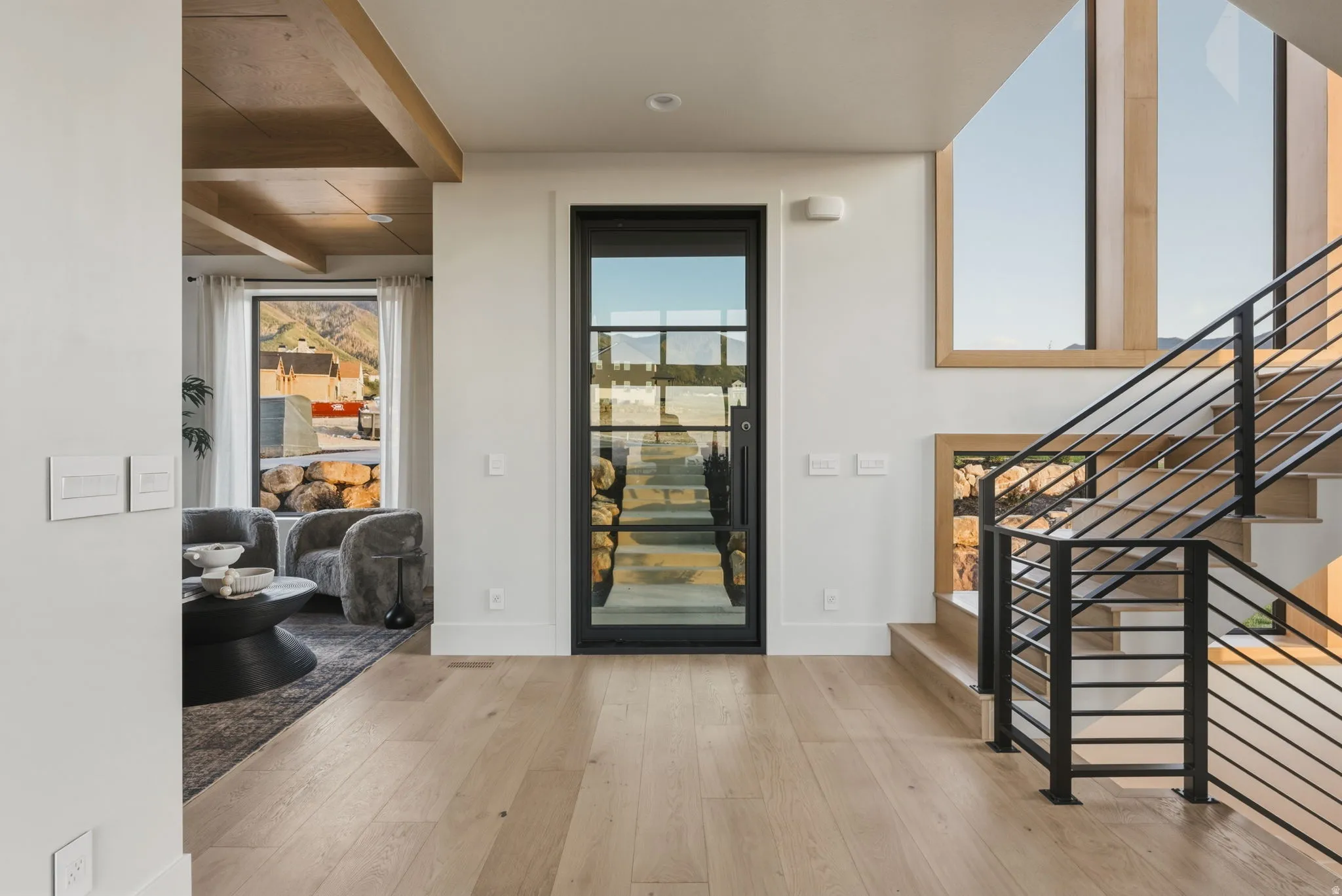 Entryway featuring a black-framed glass door, light wood-finish flooring, and a modern staircase with black metal railings