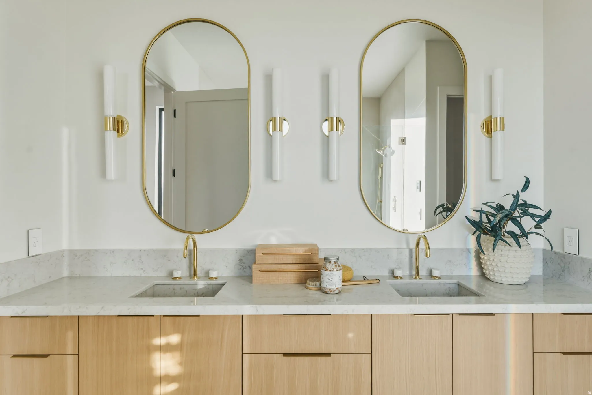Dual vanity with light wood-finish cabinetry, integrated sinks, and polished gold-tone fixtures