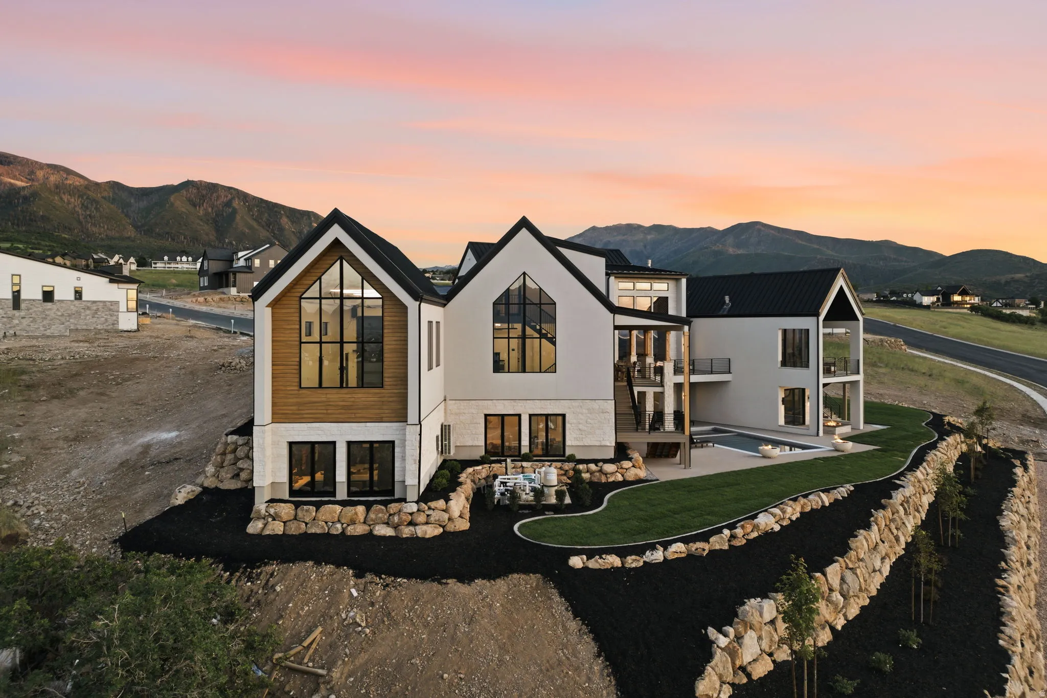Contemporary architectural style featuring expansive windows, a sleek black roof, and exterior finishes combining light-toned siding, wood paneling, and stone accents