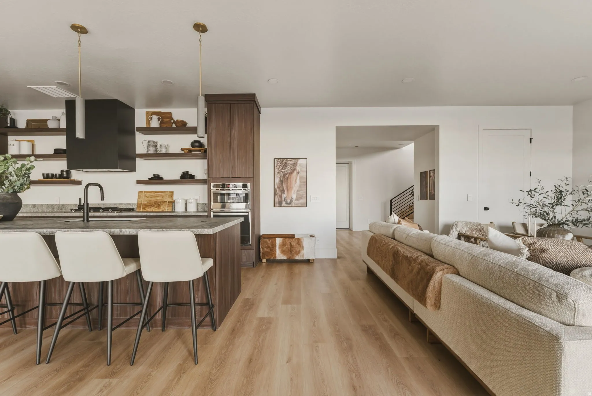 Open-concept living area featuring wood-finish flooring, a kitchen island with seating, dark wood cabinetry, integrated oven, and a modern range hood