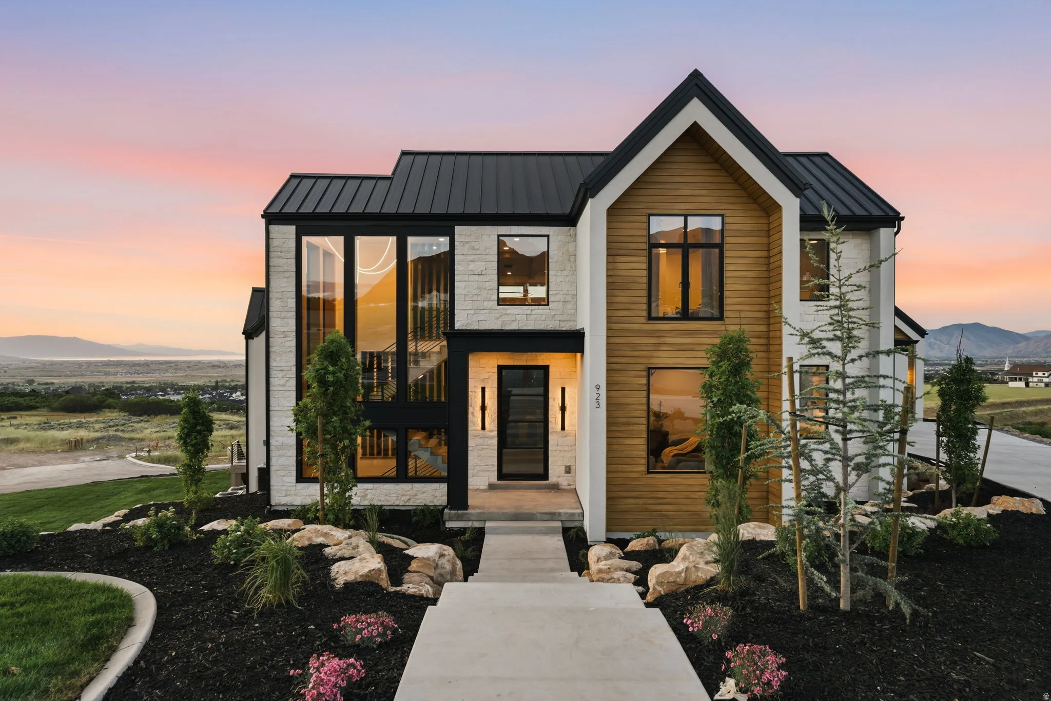 Contemporary exterior featuring a black metal roof, vertical wood-finish siding, light-colored stone veneer, and extensive black-framed windows