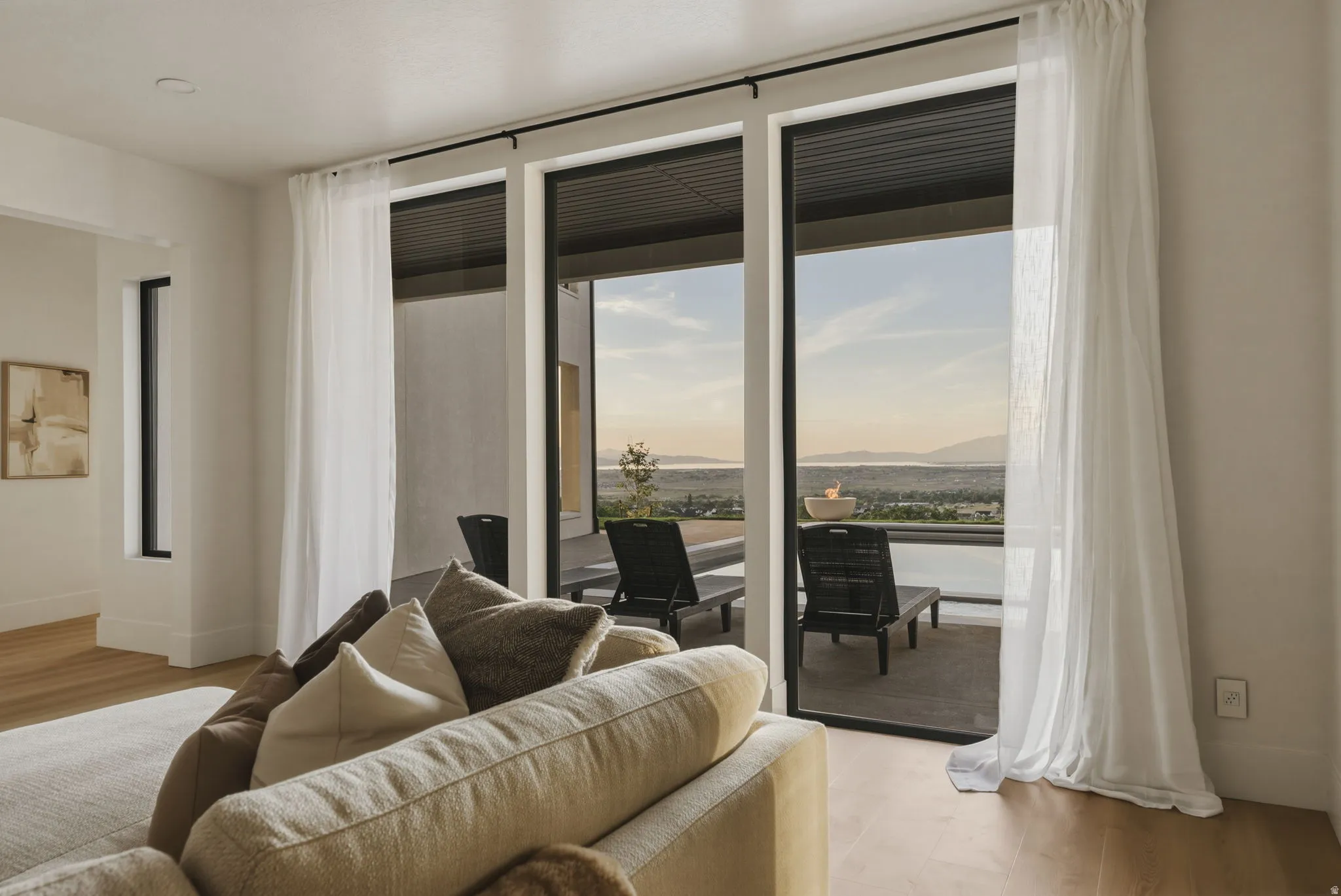 Expansive glass sliding doors with sheer drapery open to an outdoor patio with distant scenery