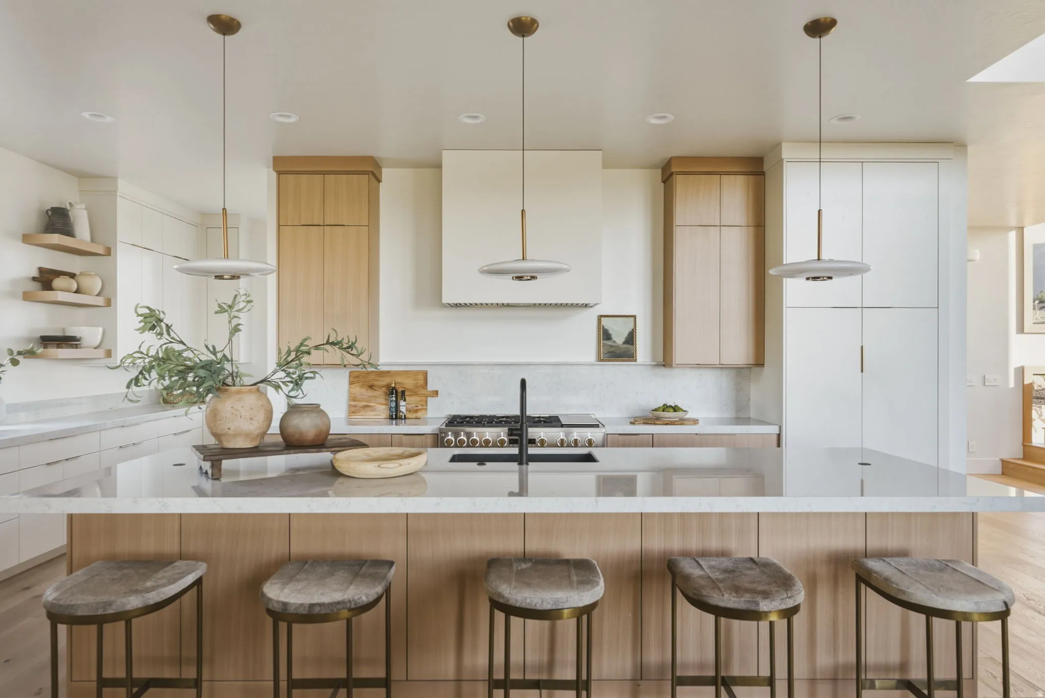 Spacious kitchen featuring a large island with seating, a gas range, integrated hood, and a combination of white and wood-finish cabinetry