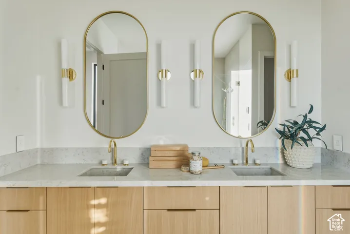 Dual vanity with light wood-finish cabinetry, integrated sinks, and polished gold-tone fixtures