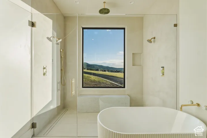 Freestanding soaking tub with fluted exterior, walk-in shower with dual shower heads, and large window showcasing mountain scenery