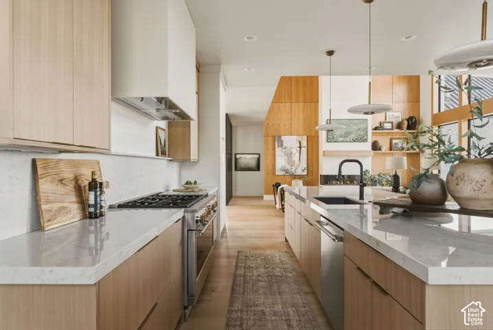 Open-concept kitchen featuring light wood-finish cabinetry, stone countertops, and a stainless steel gas range with a matching range hood