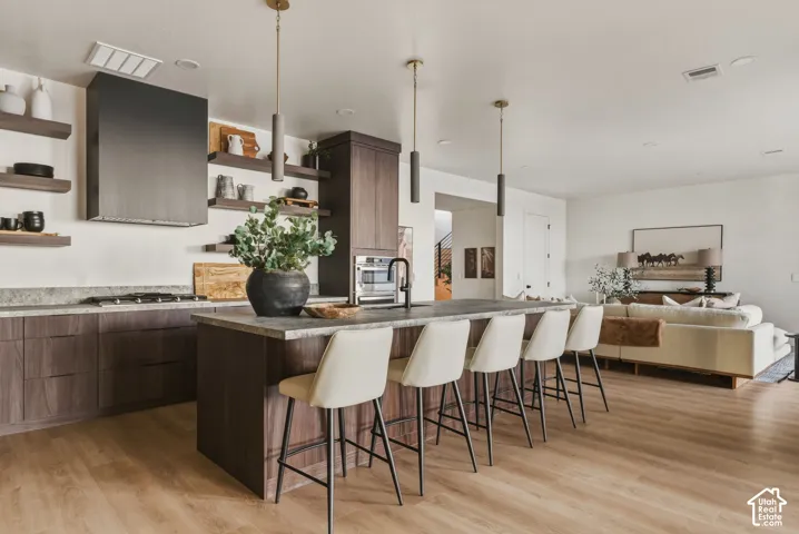 Open-concept kitchen featuring dark wood-finish cabinetry, stone countertops, a large center island with pendant lighting, and light wood-finish flooring
