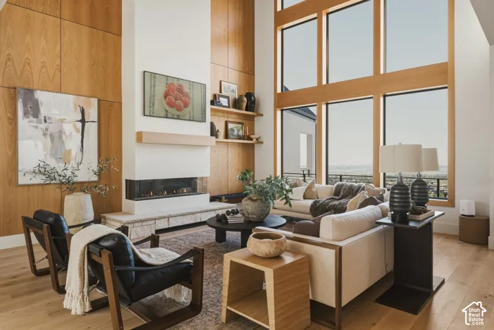 Great room featuring a contemporary linear fireplace with a stone hearth, wood-paneled accent wall, and expansive floor-to-ceiling windows with wood frames