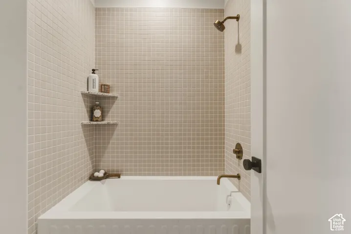 Tub and shower combination featuring floor-to-ceiling square tile, bronze-finish fixtures, and built-in corner shelving
