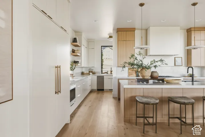 Open-concept kitchen featuring light wood-finish flooring, a central island with countertop seating, white and light wood-finish cabinetry, integrated appliances, and a range hood