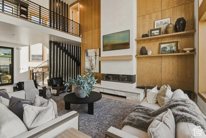 Two-story living area featuring a linear fireplace with a stone hearth, wood-paneled accent walls, and a multi-level open-tread staircase with metal railings