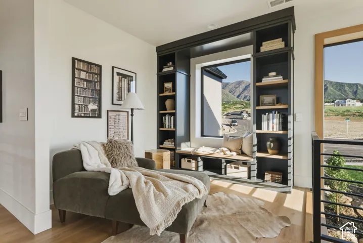 Built-in shelving unit with a window bench, light wood-finish flooring, white walls, and a black metal railing